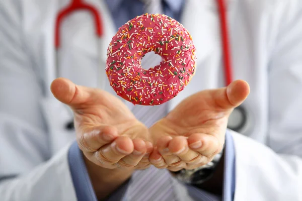 Doctor in office holding in hand pink doughnut — Stock Photo, Image