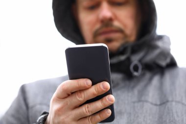 Kapüşonlu evli bir adam akıllı telefona bakar.