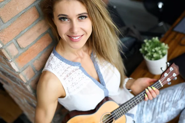 Feliz hembra sonriente sentada en la mesa jugando ukelele pequeño — Foto de Stock