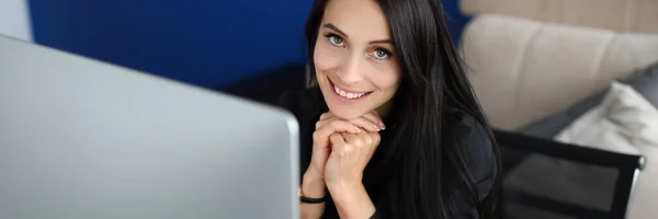 Счастливая брюнетка женщина сидит на рабочем месте и улыбается — стоковое фото