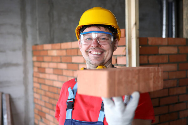Счастливый строитель держит бричку за кирпичную кладку и улыбается