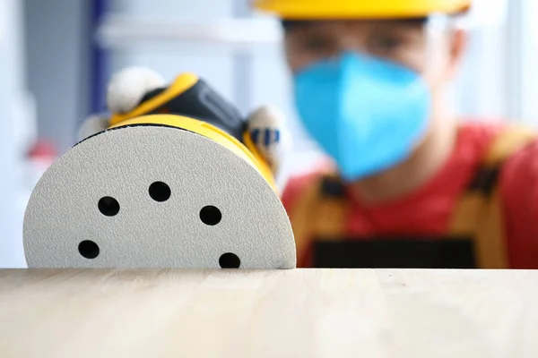 Плотник в защитной маске шлифует инструментом — стоковое фото