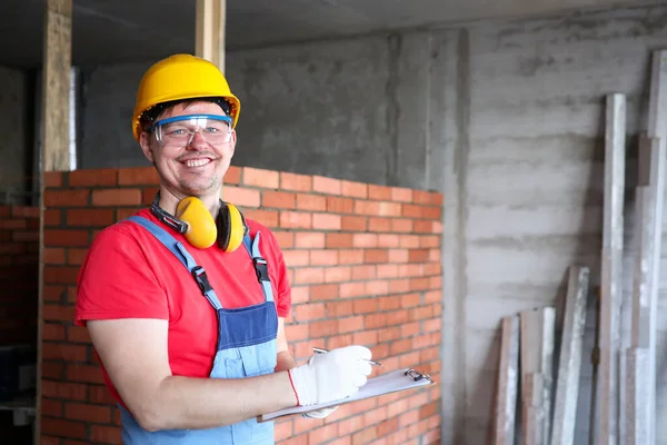 Construtor sorridente escrevendo em resultados de trabalho de área de transferência — Fotografia de Stock