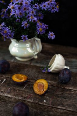 Turuncu eriğin yanında, beyaz vazoda mavi çiçekler. Büyükanne evindeki gibi ahşap masa..