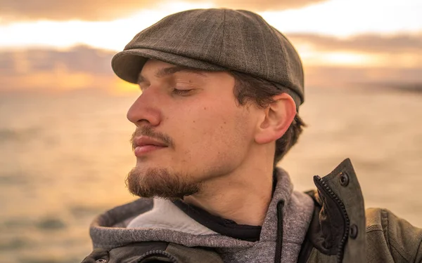 Gün batımı denizinin yanındaki şapkalı rahatlatıcı adamın selfie 'si.