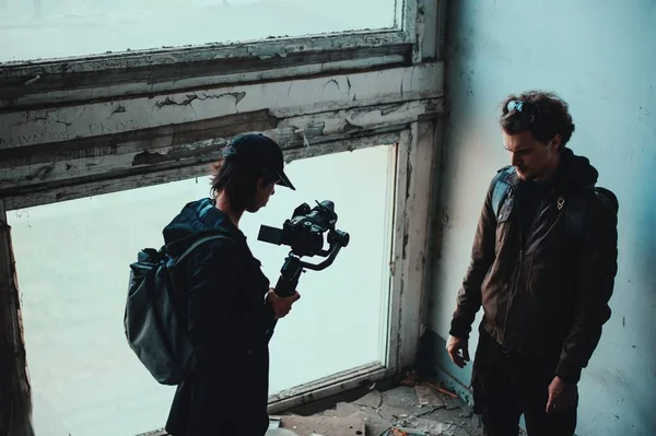 Longue chevelure opérateur filmer bouclé gars dans détruit bâtiment à la fenêtre — Photo