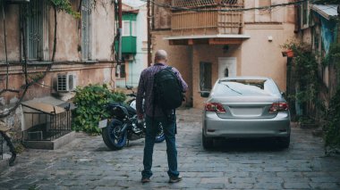 Arabanın ve moto 'nun yanındaki dar yolda kel bir adamın arkası.