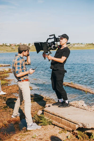 Professional operator wig rig camera shoots stylish guy on a river coast — Stock Photo, Image