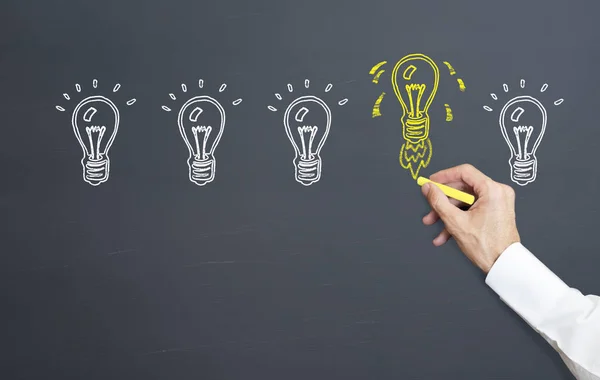 man draws idea lamp on blackboard and is flying rocket structure