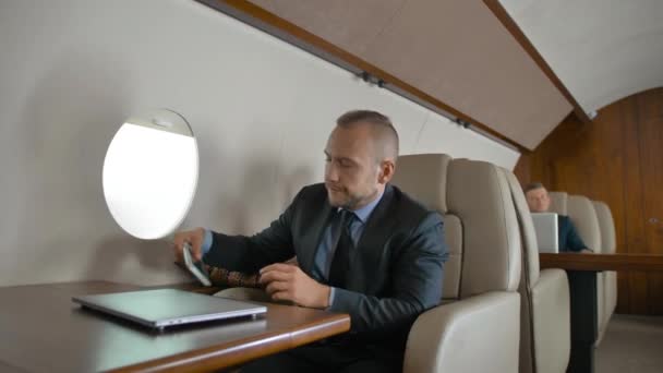 Vertrouwen zakenman in formele pak reizen op zijn prive-jet en chatten op mobiele telefoon. — Stockvideo