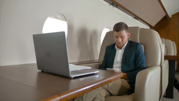 Бизнесмен болтает и сидит в кресле на частном самолете — стоковое видео