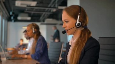 Çağrı Merkezi çalışanları anlaşma ofisinde çalışıyorum. İlk plan müşteriyle konuşurken kulaklıktaki şu yakışıklı genç kadın. Güzel manzaralı modern iş oda. 4k Ultrahd.