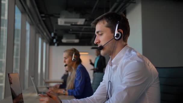 Obrero guapo en auriculares llamando a cuctomers en el centro de llamadas de oficina de negocios — Vídeo de stock