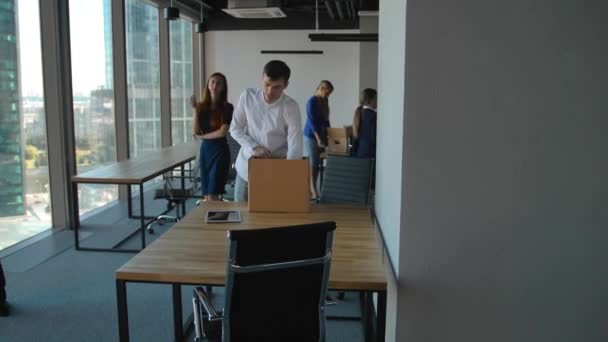 Junger Angestellter beim Auspacken einer Kiste mit Unterlagen und Ausrüstung. seine Kollegen in der Nähe im modernen Büro — Stockvideo