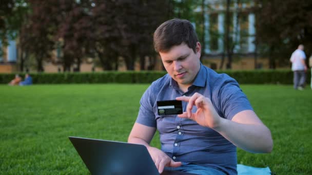 Człowiek z karty kredytowej i laptop na trawie w parku — Wideo stockowe