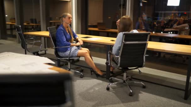Две девушки сидят в бизнес-центре, сплетничают и обсуждают бизнес-идеи — стоковое видео