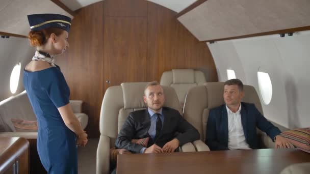 Empresarios en jet privado relajándose mientras vuelan y hablan con azafata — Vídeo de stock