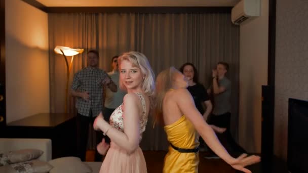 Zwei attraktive sexy Mädchen tanzen auf einer Party mit Freunden dahinter. — Stockvideo