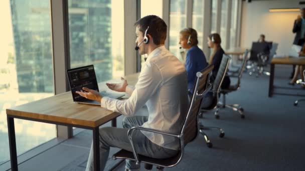 Vista posterior de los empresarios en auriculares usando computadoras portátiles mientras trabajan en la oficina — Vídeo de stock