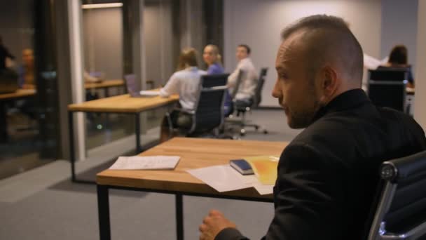 Empresario escribiendo notas en documentos sentados junto a la mesa en la oficina durante la noche, 4K — Vídeo de stock