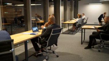 İş adamları gece geç saatlerde ofis masasında dizüstü bilgisayarları, tabletleri ve çizimleri tartışıyor ve kullanıyor.