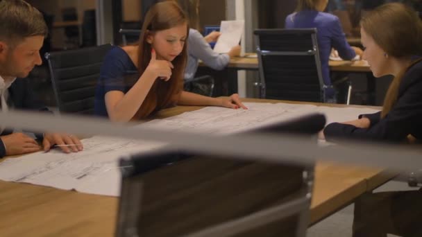 In het moderne kantoor kijken drie medewerkers aan tafel naar de krant en praten. Gooi het glazen uitzicht. — Stockvideo