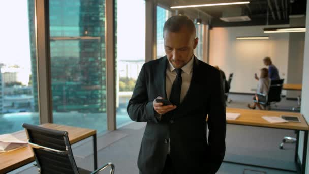 Portrait of a attractive businessman standing near window and writing sms — Stock Video