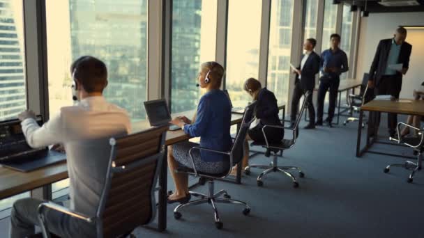 Vista posterior de joven hombre de negocios guapo y hermosas mujeres de negocios en auriculares usando computadoras portátiles mientras trabaja en la oficina — Vídeo de stock