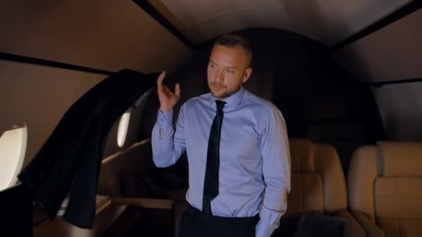 Portrait of businessman throwing a jacket on his shoulder in private jet. — Stock Video