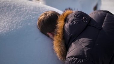 Kış lık ceketli bir adam kar akıntısında yüzünün izlerini sürüyor.