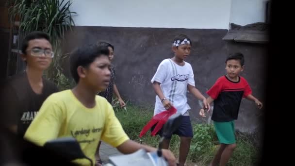 Bekymmerslös barndom. Balinesiska barn springa nedför gatan efter karnevalen — Stockvideo