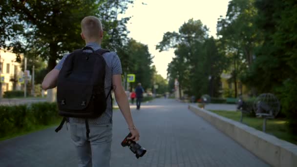 En student fotograf går längs en stadsgata bakom sig — Stockvideo