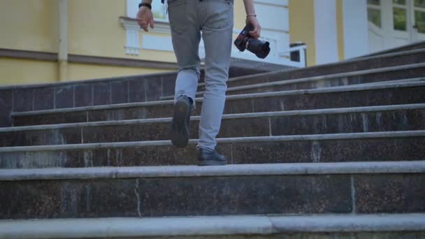 Achteraanzicht van een toeristische benen met een camera klimmen de trappen van een historisch gebouw. — Stockvideo