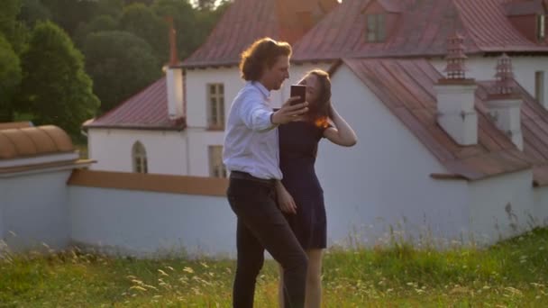 Paar neemt een selfie tegen met het Gatchinas Priory Palace in een park — Stockvideo