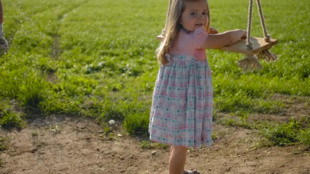 Little 3-jarige meid probeert een touw houten schommel te beklimmen — Stockvideo