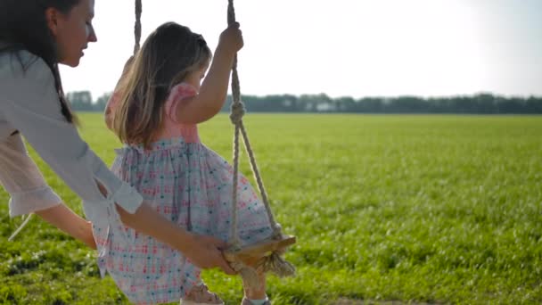 若い女性は彼女の3歳の娘がロープスイングでスイングを助けます — ストック動画