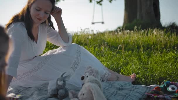 En ung mor och hennes två små döttrar gjorde en picknick i en clearing nära en ensam gammal ek — Stockvideo