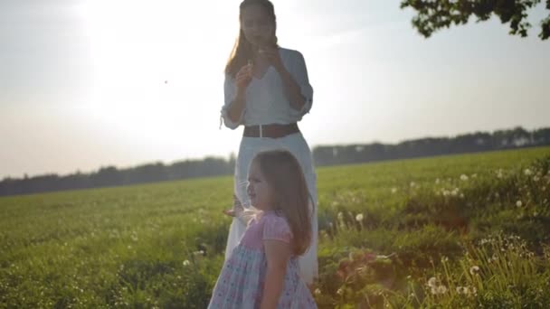 Mamá en un vestido blanco sopla burbujas de jabón para su hija pequeña — Vídeos de Stock