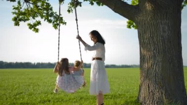 Sevimli anne eski bir ağaca bağlı bir ip salıncak kızlarını salıncak.