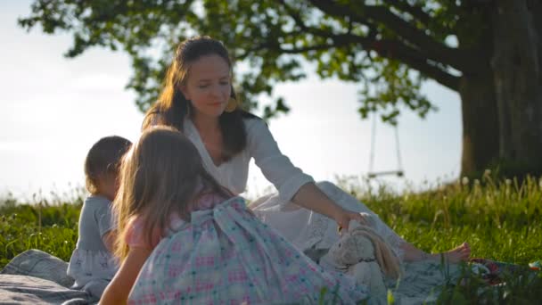 Une jeune mère et deux petites filles jouant des jouets près d'un vieux chêne solitaire — Video