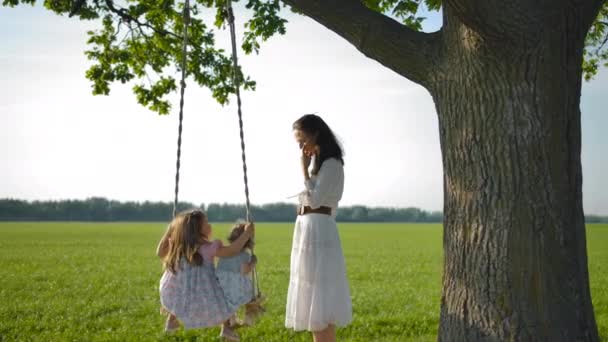 Μια νεαρή μητέρα κουνάει τις κόρες της σε μια ξύλινη κούνια. — Αρχείο Βίντεο