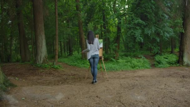 Девушка рисует пейзаж, стоящий перед мольбертом в парке — стоковое видео