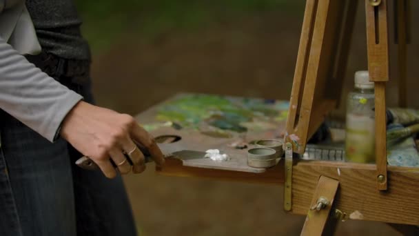 Une main de fille étalant une peinture à l'huile blanche avec une spatule sur la palette . — Video