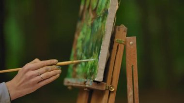 Plenar bir manzara boyama bir fırça ile bir kadın el yakın çekim.