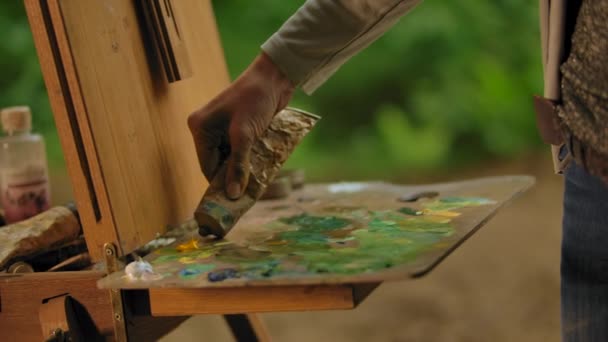 Woman artist squeezing a tube with yellow orange oil paint on a palette. — Stockvideo