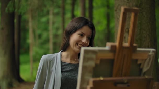 Chica artista pintando un cuadro en el bosque y hablando por teléfono móvil — Vídeos de Stock