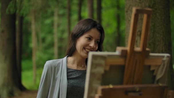 Girl artist painting a picture in the forest and talking by mobile phone — Stock Video