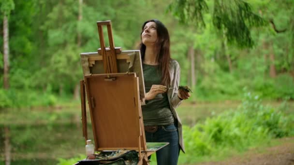 Vista centrale di una bella donna bruna che dipinge un quadro su tela in un parco — Video Stock