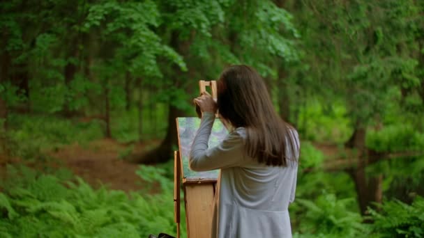 Вид спереду молодої жінки-художниці, яка малює пейзаж в літньому лісі — стокове відео