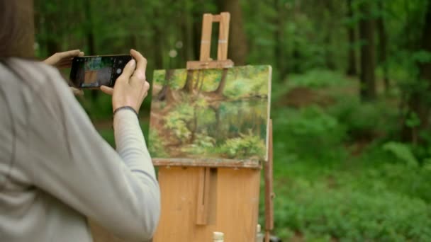 Задний вид брюнетки женского рисует пейзаж на открытом воздухе в лесу и фотографирует — стоковое видео